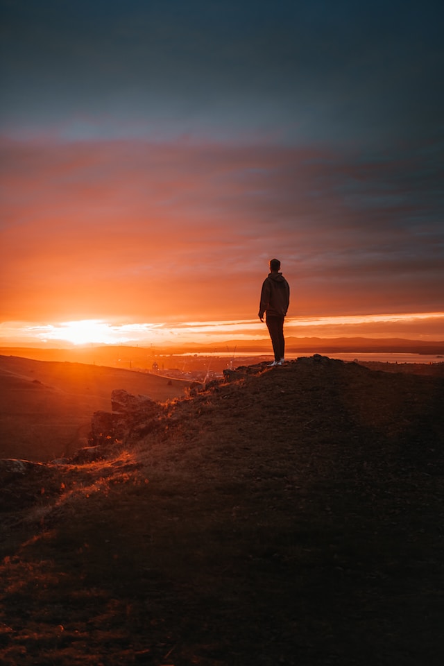 Person standing on an elevated landscape overlooking a sunset/sunrise.